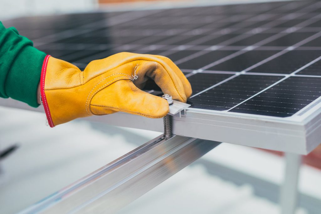 pexels-photo-8853500 Close-up of a worker's hand with protective gloves adjusting a bolt on a solar panel.
